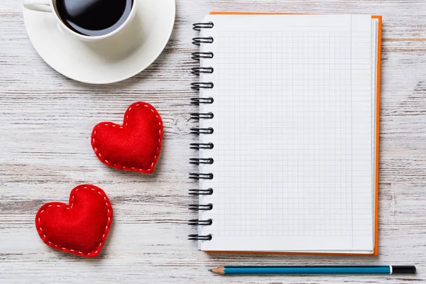 Coffee cup notepad pencil and two red hearts on wooden surface