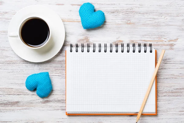 Coffee cup notepad pencil and two hearts on wooden surface