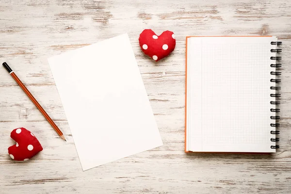 Hearts and blank notepad with pencil on wooden table