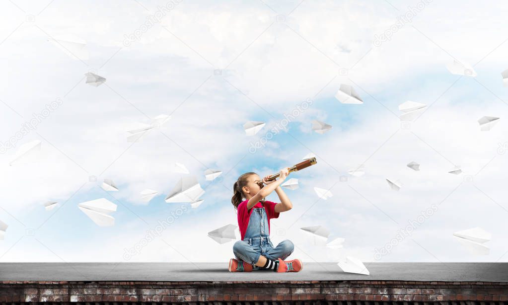 Cute kid girl sitting on house roof and looking in spyglass