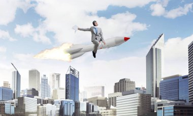 Arka plan üzerinde modern cityscape gökdelenler ve mavi gökyüzü ile roket üzerinde uçan takım elbiseli Genç ve mutlu işadamı kavramsal görüntü.