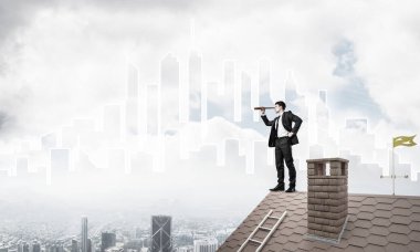 Çatıda takım elbiseli genç bir işadamı var. Karışık ortam