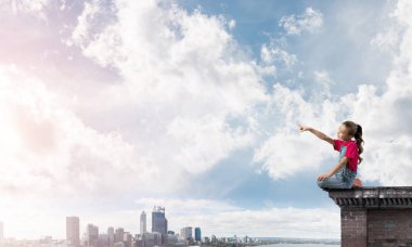 Üstte oturan ve bir şeyi işaret eden sevimli bir kız.