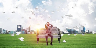 Hüsrana uğramış işadamı bankta oturuyor ve elleriyle kulaklarını kapatıyor.