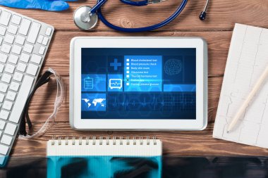 Beyaz tablet bilgisayar ve doktor aletleri ahşap masada.