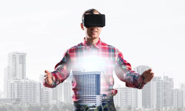 Sanal gerçeklik kulaklığı olan genç bir adam ya da şehrin arka planında 3 boyutlu gözlüklü.