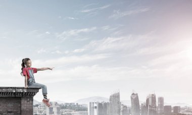 Üstte oturan ve bir şeyi işaret eden sevimli bir kız.