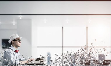 Genç yazar şapka ve gözlük kapalı uçan harfler arasında ve arka plan üzerinde office manzaralı masada otururken yazarak makinasıyla adam.