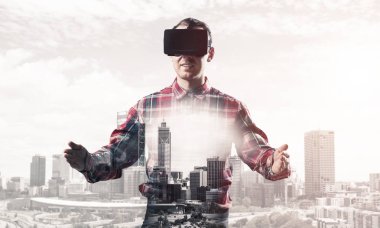 Sanal gerçeklik kulaklığı olan genç bir adam ya da şehrin arka planında 3 boyutlu gözlüklü.
