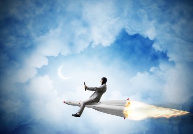 Zemin üzerine mavi gece gökyüzü bulutlar ve ay ile roket üzerinde uçan takım elbiseli genç işadamı kavramsal görüntü.