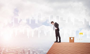 Genç işadamı tuğladan çatının kenarında dikilip aşağıya bakıyor. Karışık ortam