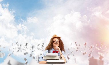 Genç ve güzel bir kadın yazar şapka ve gözlük kağıtları ile bulutlu gökyüzü arka plan üzerinde uçan arasında masadaki otururken yazarak makinasıyla.