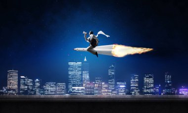 Arka plan üzerinde gece cityscape ve mavi gökyüzü ile roket üzerinde uçan takım elbiseli genç işadamı kavramsal görüntü.