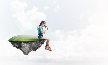 Gökyüzünde yüzen bir adada oturan tatlı, gülümseyen bir kız.