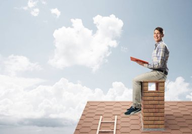 Elinde kırmızı kitap ile evin baca rahat oturan genç adam