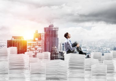 Düşünceli işadamı uzak belgeler cityscape ve arka plan üzerinde güneş ışığı ile yığını üzerinde otururken arıyorum. Karışık teknik.