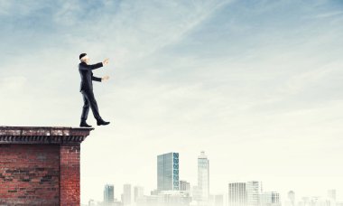 Binanın tepesinde gözü kapalı yürüyen bir iş adamı.