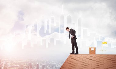 Genç işadamı tuğladan çatının kenarında dikilip aşağıya bakıyor. Karışık ortam