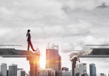 Gizli tehditlerin ve risklerin sembolü olarak beton köprüde gözü kapalı yürüyen bir iş adamı. Arka planda güneş ışığı olan şehir manzarası. 3B görüntüleme.