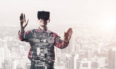 Sanal gerçeklik kulaklığı olan genç bir adam ya da şehrin arka planında 3 boyutlu gözlüklü.