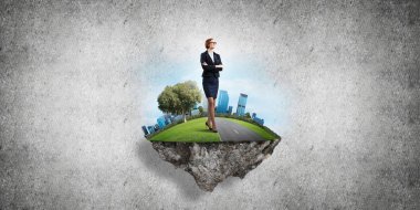 Yeşil yüzen adada beton zemine karşı duran kendine güvenen zarif bir iş kadını.