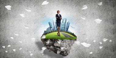 Yeşil yüzen adada beton zemine karşı duran kendine güvenen zarif bir iş kadını.