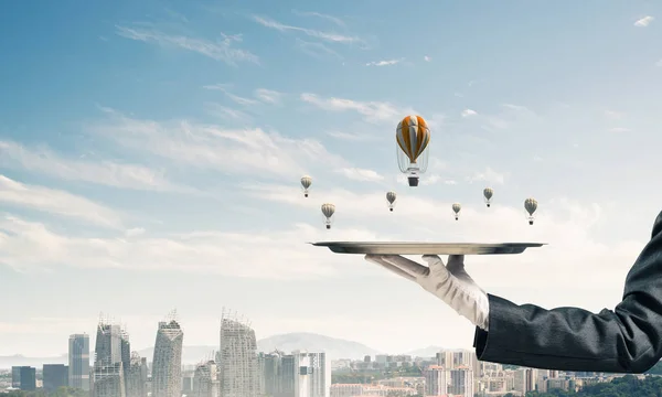 Closeup of waitress\'s hand in glove presenting flying aerostats on metal tray with modern cityscape view on background. 3D rendering.