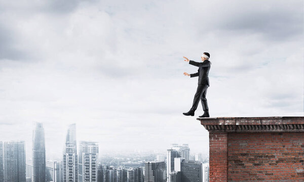 Businessman with blindfolder on eyes walking on building top
