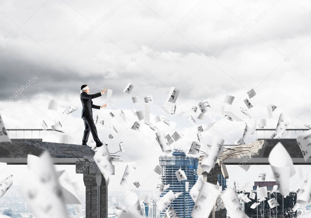 Businessman walking blindfolded among flying papers on concrete bridge with huge gap as symbol of hidden threats and risks. Cityscape view on background. 3D rendering.