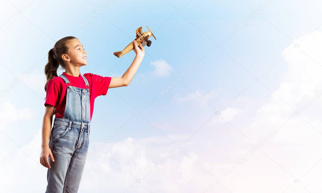 Cute kid girl in overalss with retro plane model in hand
