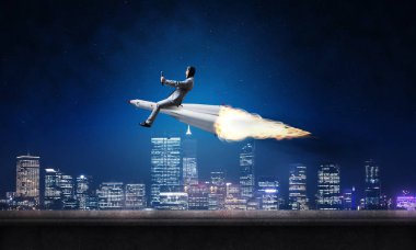 Arka plan üzerinde gece cityscape ve mavi gökyüzü ile roket üzerinde uçan takım elbiseli genç işadamı kavramsal görüntü.