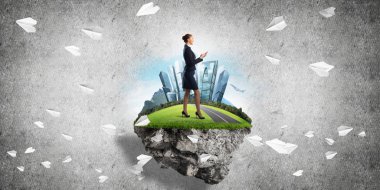 Yeşil yüzen adada beton zemine karşı duran kendine güvenen zarif bir iş kadını.