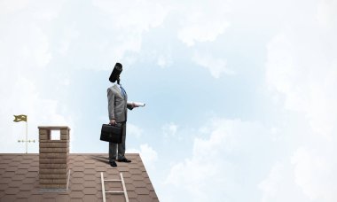 Evin çatısında baş durmak yerine kamerayla zum yapan yüzü olmayan bir iş adamı.