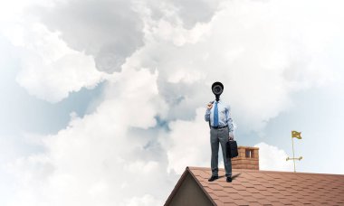 Evin çatısında baş durmak yerine kamerayla zum yapan yüzü olmayan bir iş adamı.