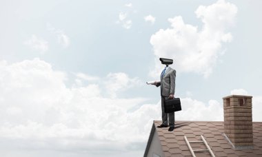 Evin çatısında baş durmak yerine kamerayla zum yapan yüzü olmayan bir iş adamı.