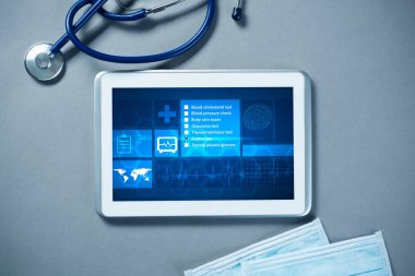 Gri yüzeyde beyaz tablet ve doktor araçları