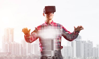 Sanal gerçeklik kulaklığı olan genç bir adam ya da şehrin arka planında 3 boyutlu gözlüklü.