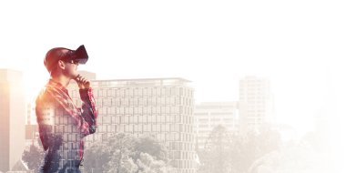 Sanal gerçeklik kulaklığı olan genç bir adam ya da şehrin arka planında 3 boyutlu gözlüklü.