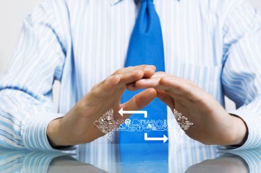 Masada oturan takım elbiseli bir işadamı avuçlarıyla koruyucu hareketler yapıyor.