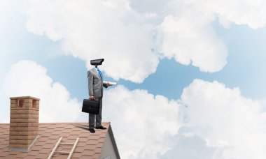 Evin çatısında baş durmak yerine kamerayla zum yapan yüzü olmayan bir iş adamı.