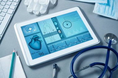 Gri yüzeyde beyaz tablet ve doktor araçları