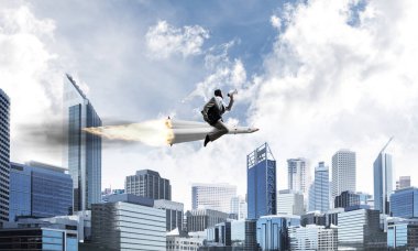 Arka plan üzerinde modern cityscape gökdelenler ve mavi gökyüzü ile roket üzerinde uçan takım elbiseli genç işadamı kavramsal görüntü.