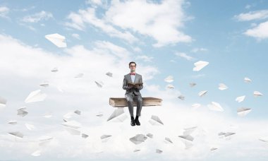 Komik adam kırmızı gözlük ve etrafında uçan kitap ve kağıt uçaklar üzerinde oturan takım elbise