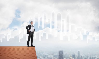 Kararlı genç işadamı evin çatısında dikiliyor ve başka tarafa bakıyor. Karışık ortam