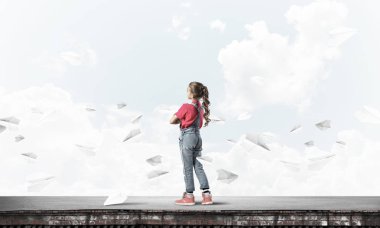 Sevimli kız etrafında uçan çatı ve kağıt uçaklar binasında ayakta