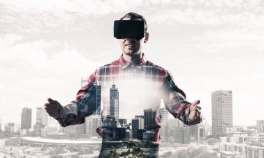 Sanal gerçeklik kulaklığı olan genç bir adam ya da şehrin arka planında 3 boyutlu gözlüklü.