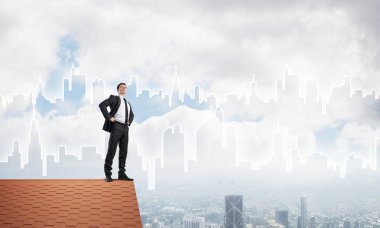 Kararlı genç işadamı evin çatısında dikiliyor ve başka tarafa bakıyor. Karışık ortam