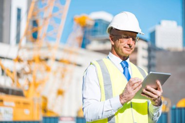Kıdemli mühendis erkek takım elbise ve tablet PC'de çalışma kask