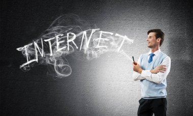 Akıllı-casual giyim gri karanlık duvar ve duman arka plan üzerinde yapılan internet kelime karşı dururken pipo kendinden emin ve genç işadamı yatay çekim.