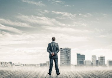 İşadamı arkası dönük duruyor ve şehir manzarasına bakıyor.